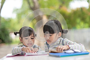 Two student little Asian girls reading the book on table