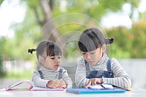 Two student little Asian girls reading the book on table