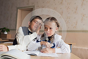 Two students a boy and a girl sit at a Desk at school and communicate with each other in the ear