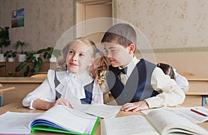Two students a boy and a girl sit at a Desk at school and communicate with each other in the ear
