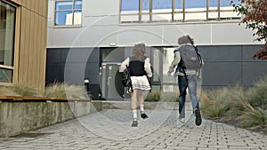 Two students, a girl and a guy, are running around the courtyard of the educational institution. Classmates are in a