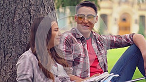 Two students leaned on a tree talking reading a book