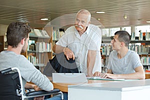 Two students reading in library with senior teacher