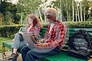 Two students studying on the bench in summer park