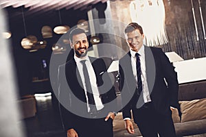 Two stylish men smiling while standing in the hall together