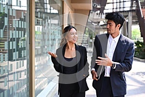 Two business colleagues having a discussion while walking outside modern office building.