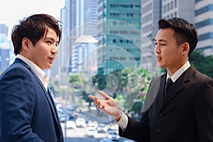 Two successful businessmen in suit talking and discussing at modern city downtown with skyscraper building as blurred background,