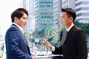 Two successful businessmen in suit talking and discussing at modern city downtown with skyscraper building as blurred background,