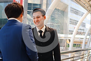 Two successful businessmen in suit talking and discussing at modern city downtown with skyscraper building as blurred background,