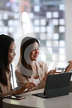 Two successful businesswomen discussing company financial strategy while sitting in meeting room.