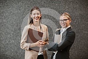 Two successful businesswomen holding digital tablet and clipboard, looking at camera