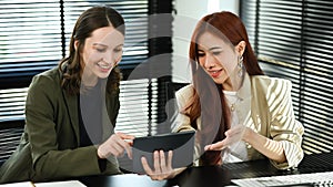 Two successful businesswomen using digital tablet, collaborating and planning for innovation