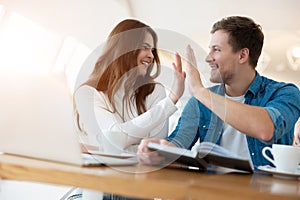 Two successful colleagues brunette woman and handsome man giving each other high five while working in laptop during lunch break