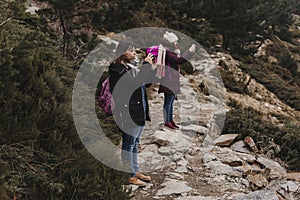 Two successful hiker woman friends enjoy the view on mountain peak. Happy backpackers in nature taking pictures with mobile phone