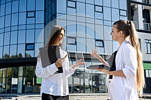 Two successful and young business ladies with tablet standing near office building