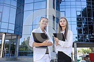 Two successful and young business ladies with tablet standing near office building