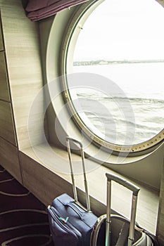 Two suitcases for traveling in front of the round porthole of the ship, the concept of leisure or business trip