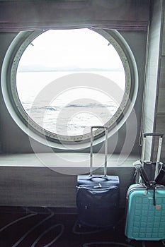 Two suitcases for traveling in front of the round porthole of the ship, the concept of leisure or business trip