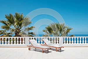 Two sun beds on villa terrace with ocean and palm tree background