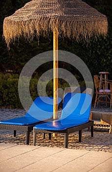 Two sun loungers and a straw beach umbrella near a swimming pool