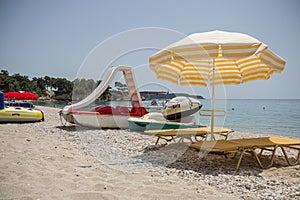 Two sunbeds with mattresses stand on the sand in the shade of a sun umbrella.