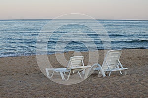 Two sunbeds on a sandy calm beach with turquoise sea water and white sand