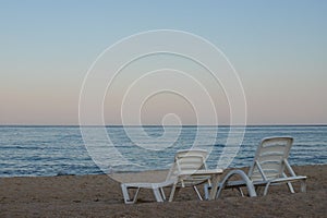 Two sunbeds on a sandy calm beach with turquoise sea water and white sand