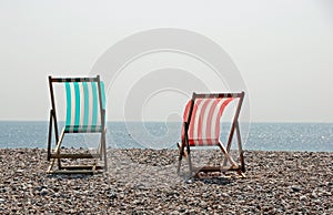 Two sunlit deckchairs on a pebble beach