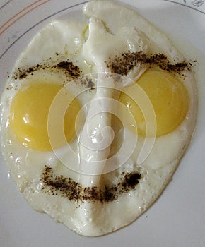 Two sunny side up fried eggs cooked like a human face with two eyes with egg yolks, eyebrows and lips are made and nose