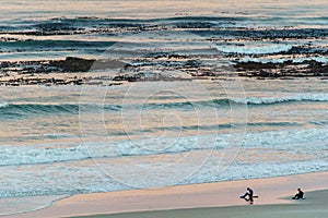 Two surfers sitting on Betty`s Bay beach at sunset in the Western Cape, South Africa