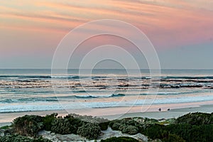 Two surfers sitting on Betty`s Bay beach at sunset in the Western Cape, South Africa