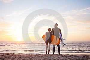 Two surfers hugging stand on sand watching the sunset over ocean photo