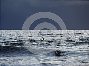 Two surfers under the storm swimming