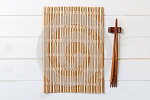 Two sushi chopsticks with empty bamboo mat or wood plate on wooden Background Top view with copy stace