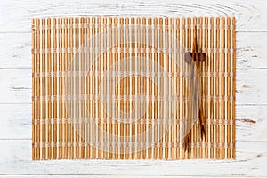 Two sushi chopsticks with empty brown bamboo mat or wood plate on white wooden Background Top view with copy space. empty asian