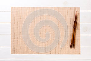 Two sushi chopsticks with empty brown bamboo mat or wood plate on white wooden Background Top view with copy space. empty asian