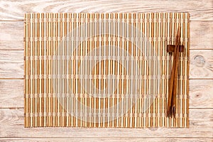 Two sushi chopsticks with empty brown bamboo mat or wood plate on brown wooden Background Top view with copy space. empty asian