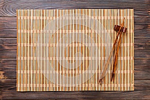 Two sushi chopsticks with empty brown bamboo mat or wood plate on wooden Background Top view with copy space. empty asian food