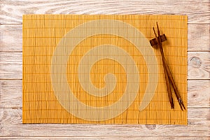 Two sushi chopsticks with empty yellow bamboo mat or wood plate on brown wooden Background Top view with copy space. empty asian