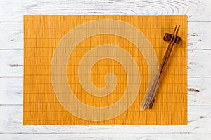 Two sushi chopsticks with empty yellow bamboo mat or wood plate on white wooden Background Top view with copy space. empty asian