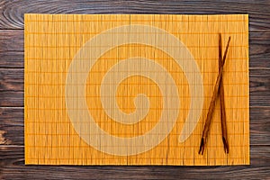 Two sushi chopsticks with yellow empty bamboo mat or wood plate on wooden Background Top view with copy space. empty asian food