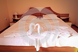 Two swans made of towels forming heart shape on bed in honeymoon suite room hotel decorated