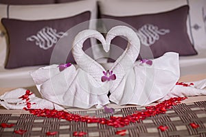Two swans made from towels are kissing on honeymoon white bed.