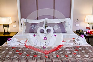 Two swans made from towels are kissing on honeymoon white bed.