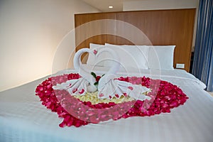 Two swans made from towels are kissing on honeymoon white bed.