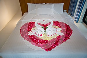 Two swans made from towels are kissing on honeymoon white bed.