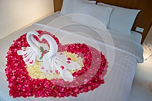 Two swans made from towels are kissing on honeymoon white bed.