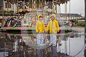 Two sweet children, boy brothers, watching carousel in the rain,