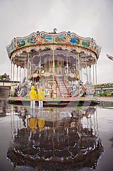 Two sweet children, boy brothers, watching carousel in the rain,