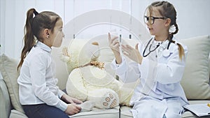 Two sweet kids playing with teddy-bear. The girl who plays a doctor is examining plush bear with stethoscope, talking